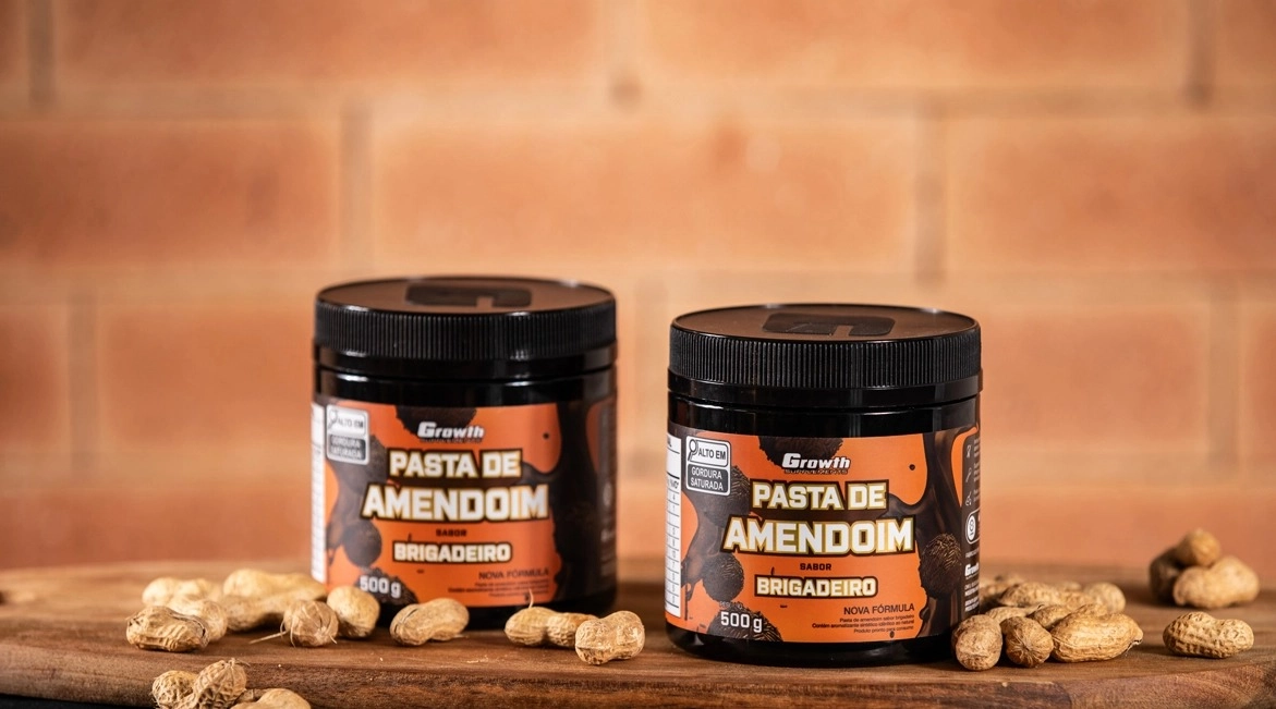 GROWTH SUPPLEMENTS - Embalagens de Pasta de Amendoim sabor brigadeiro em mesa com amendoins em volta