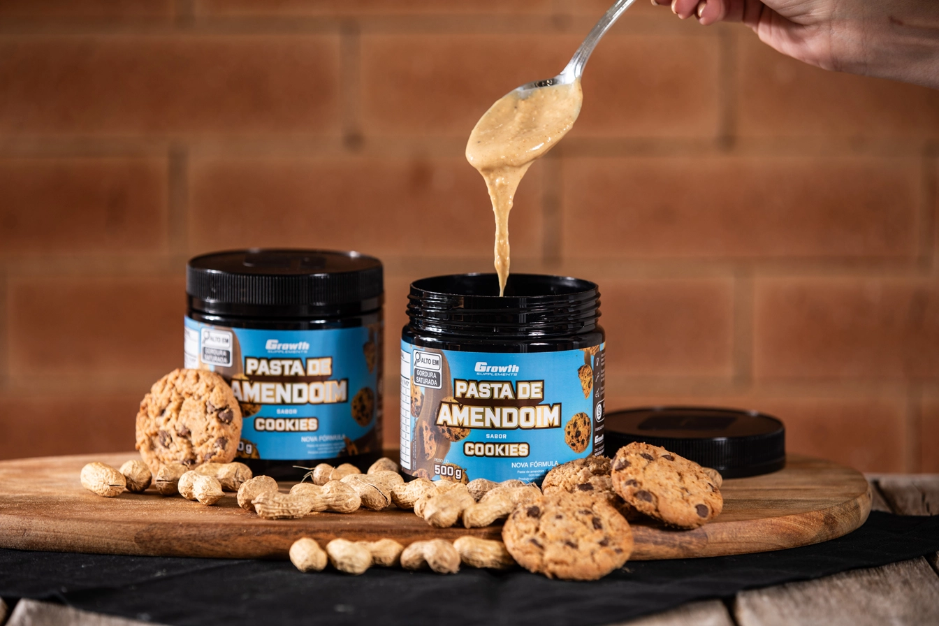 GROWTH SUPPLEMENTS - Embalagens de Pasta de Amendoim sabor brigadeiro em mesa com amendoins em volta e colher