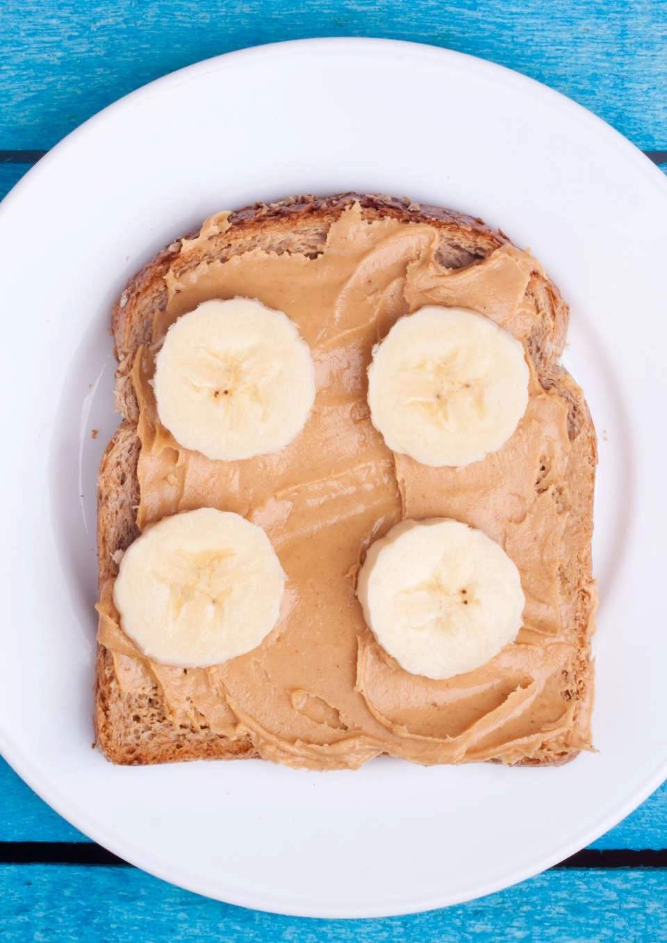 Pasta de amendoim sabor banana em uma fatia de pão de forma integral em cima de um prato branco
